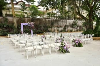 outdoor wedding setup with white chairs purple floral decorations and draped arch in a garden setting
