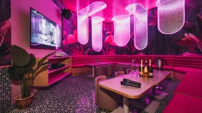 karaoke room with neon pink lighting tropical wall design round tables and champagne bottles