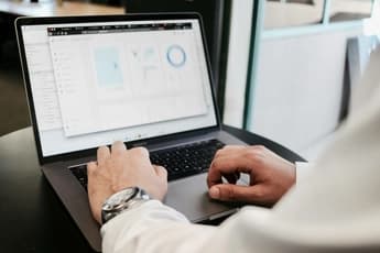 lose-up of a person's hands typing on a laptop displaying analytics and charts on a screen in an office setting