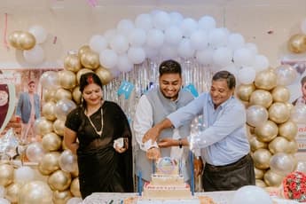 birthday celebrant cutting cake with family in front of gold and white balloon arch