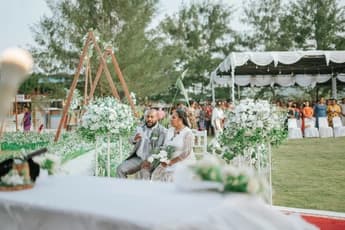 groom reading from a piece of paper beside bride holding bouquet in decorated garden setup with white drapes and flower stands
