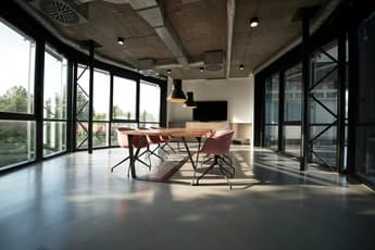 wooden table with pink chairs and ceiling lamps inside meeting room with floor to ceiling windows