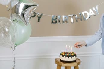 five kids wearing party hats gathered around birthday cake with decorations and golden streamers indoors