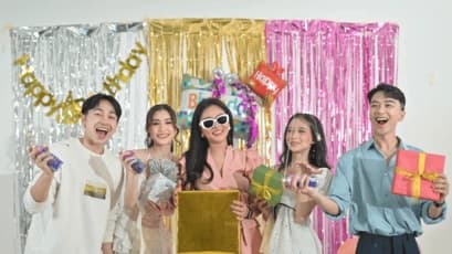 Group of friends celebrating a birthday party in KL with gifts, party poppers, and colorful backdrop decorations