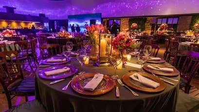An upscale corporate banquet hall featuring round dinner tables with copper charger plates and candlelight, set under an immersive purple galaxy-inspired ceiling projection for a 2026 company annual dinner.