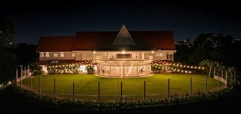 The illuminated exterior of a grand, colonial-style mansion with a spacious green lawn at night, showcasing a premier corporate event venue in Kuala Lumpur.