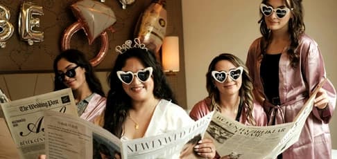 Group of women celebrating a bachelorette party, with the bride wearing a tiara and heart-shaped sunglasses and bridesmaids in matching pink robes