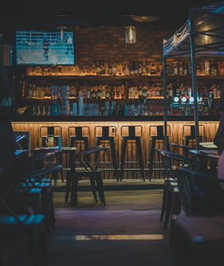 bar counter with high stools shelves of liquor bottles and tv screen in dimly lit venue