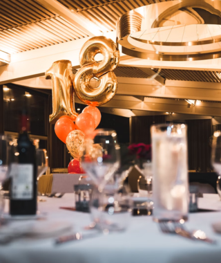 table setting with wine glasses candles and gold number balloons for 18th birthday in a decorated indoor venue