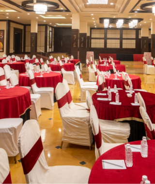 rows of round tables covered in red cloth with white chairs set up for an indoor event in a ballroom with chandeliers