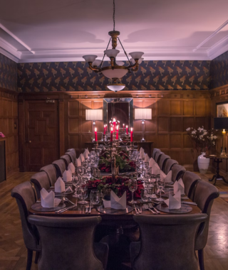 long dining table with formal table setting and candles in classic wood-paneled room with warm lighting
