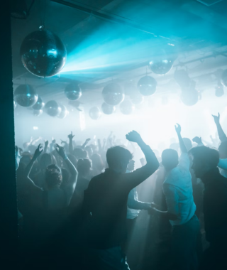 people standing and dancing under neon lights in dark indoor venue with unique ceiling decorations