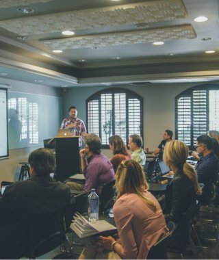 small group training session with speaker at podium and attendees facing a projected screen in a classroom