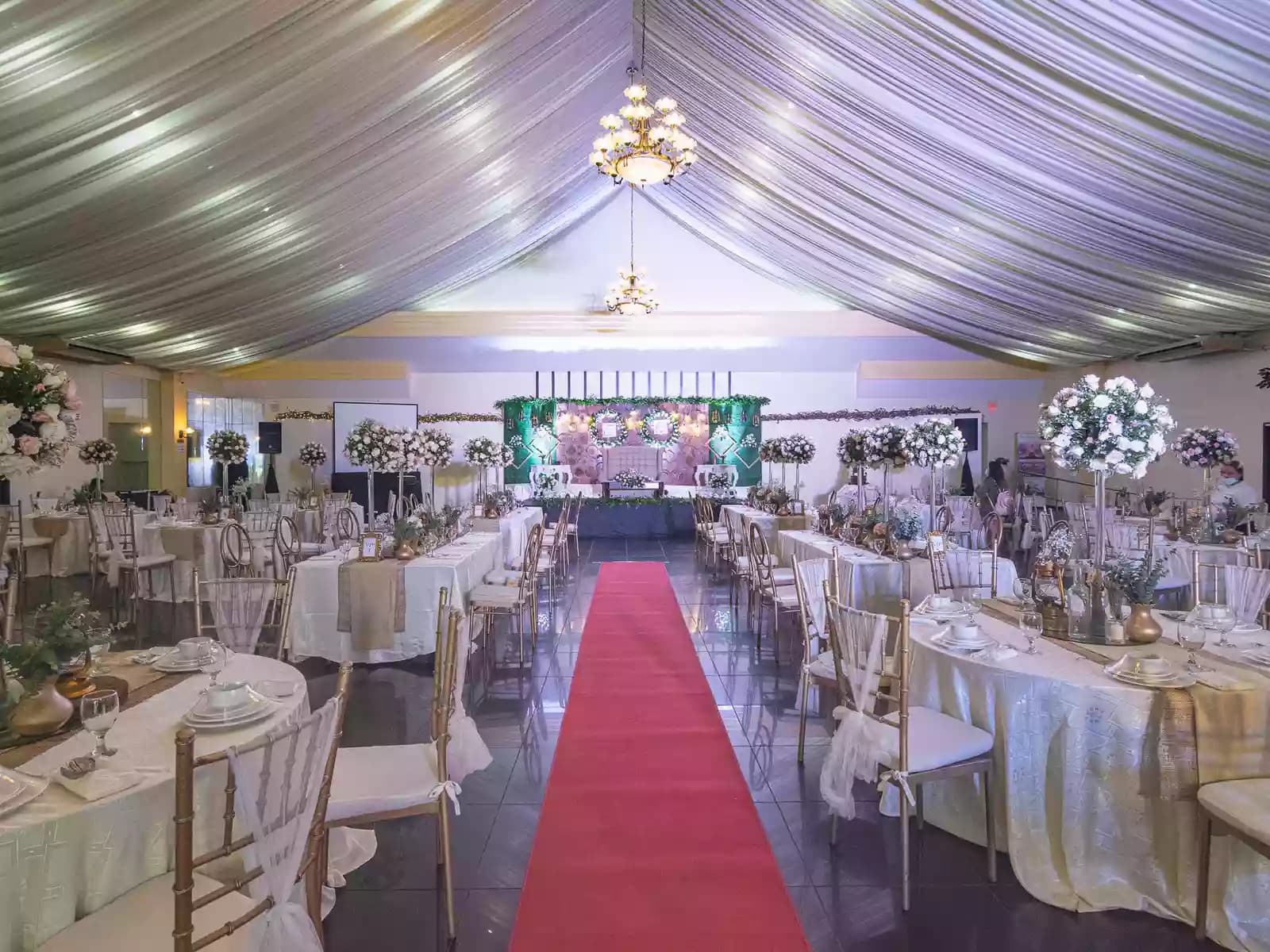 wedding reception event venue for rent in pasay philippines with white round tables and floral center pieces and red carpet laeding to stage