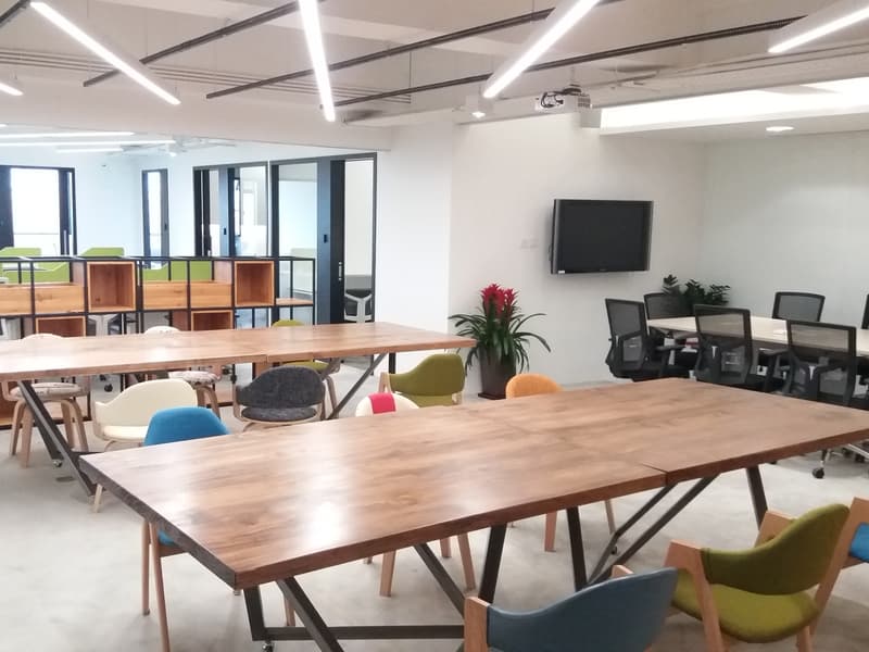coworking space area usin long wooden table and colourful chairs
