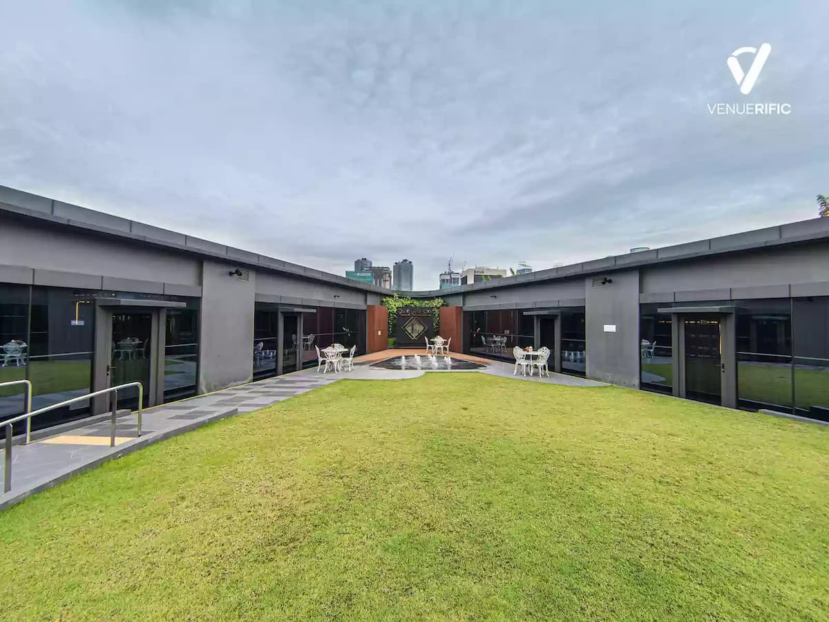 Far view of fountain in the middle of outdoor space with white chairs around tables on the side