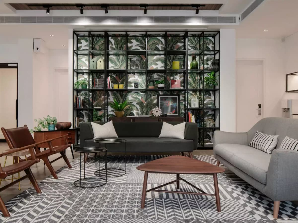 modern lounge space with a black sofa, gray armchair, wooden chairs, and a large bookshelf with plants and books