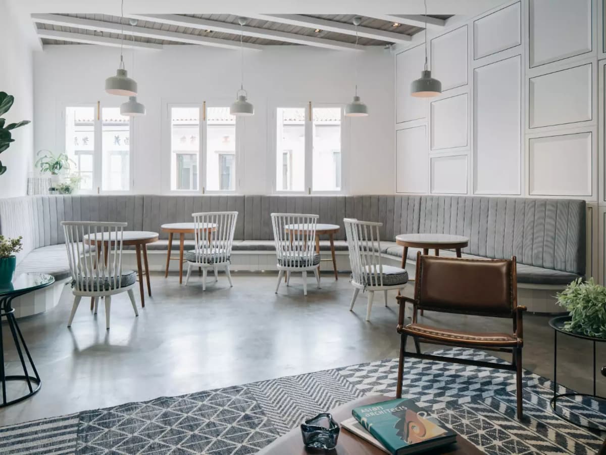 modern seating arrangement with white chairs, round tables, geometric-patterned rug, and light-colored walls