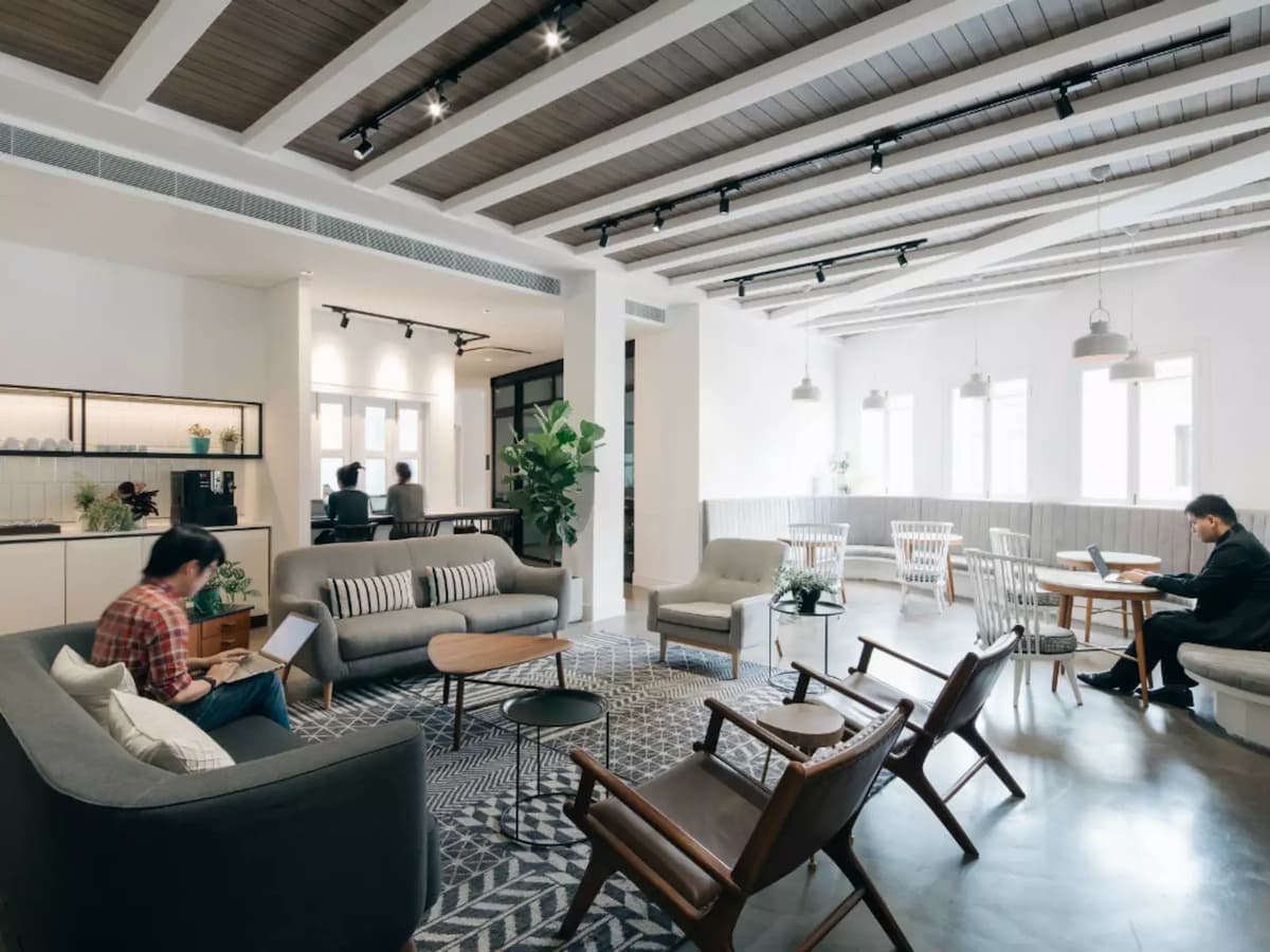 open lounge area featuring gray sofas, wooden chairs, and people working on laptops in a casual meeting space