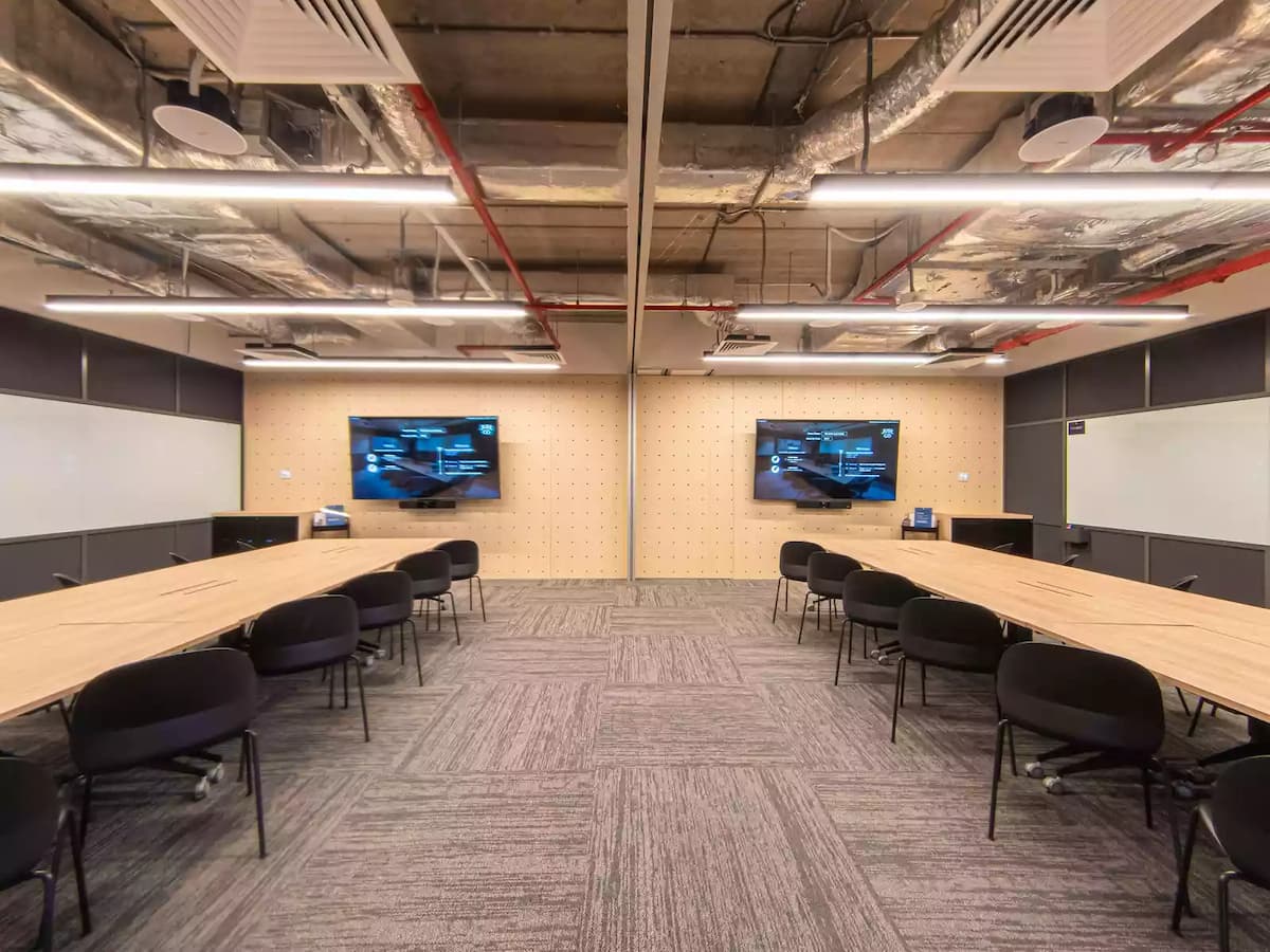 spacious and modern meeting room with two long tables, chairs, and screens