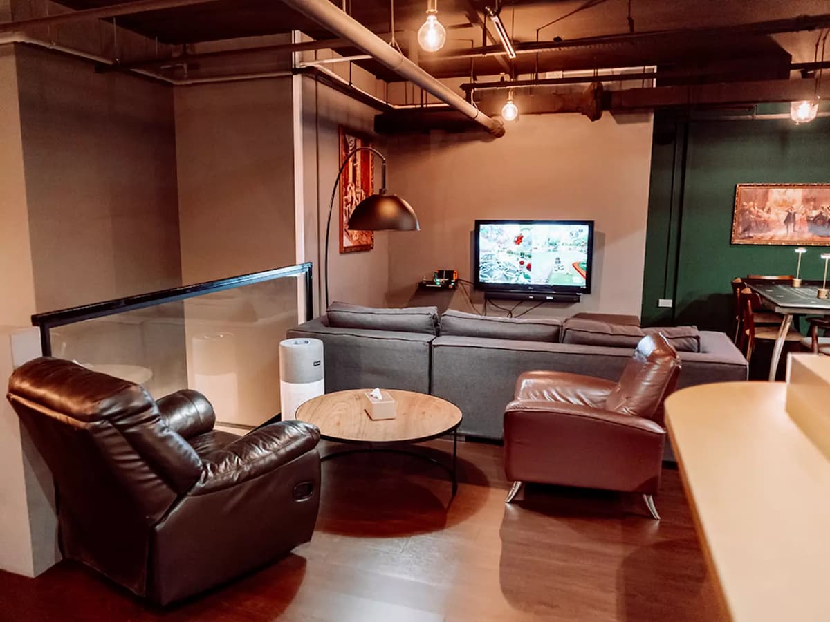 lounge area with grey modular sofa, brown leather recliners, a flat-screen TV, round coffee table, and industrial exposed pipe ceiling with Edison bulb lighting