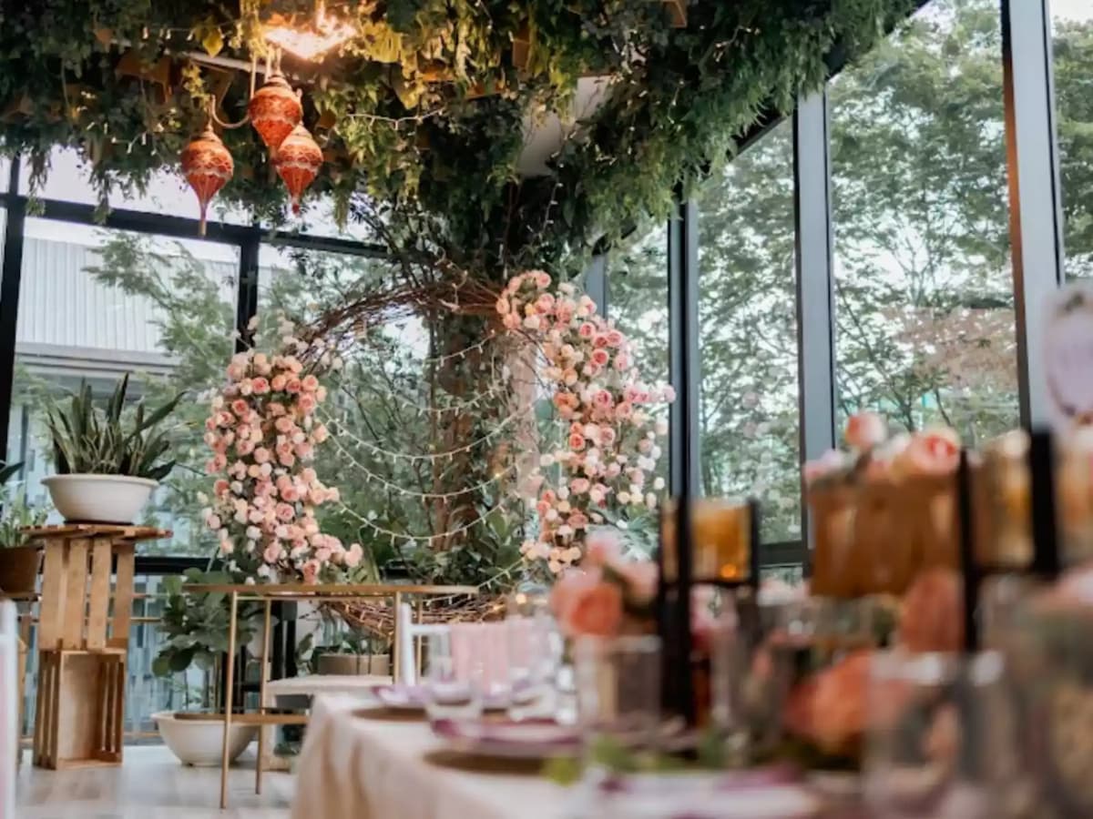 Indoor wedding venue with pink floral arch, hanging greenery, and elegantly set banquet table.