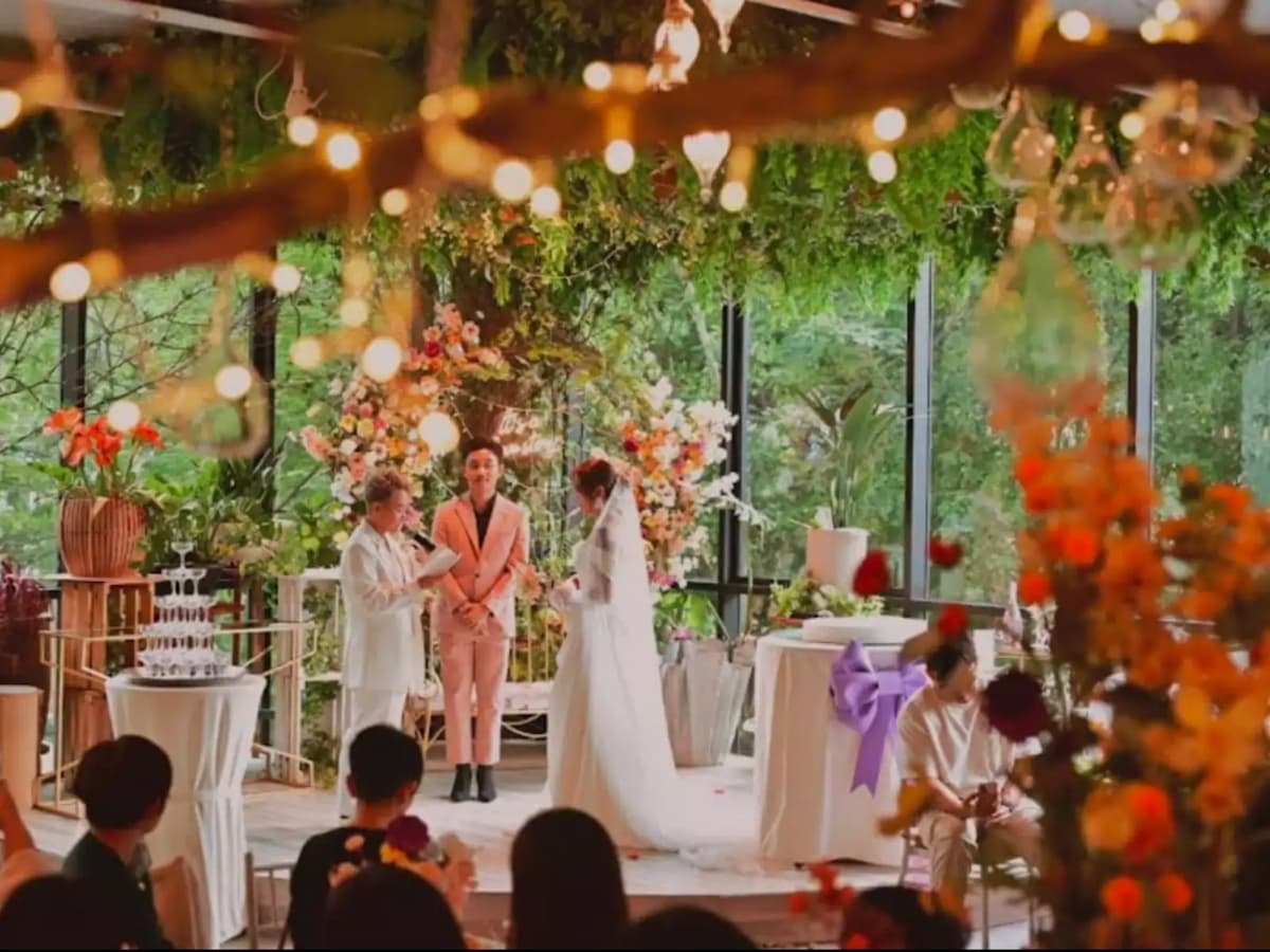 Romantic indoor wedding ceremony with floral arch, greenery ceiling decor, and warm string lights.