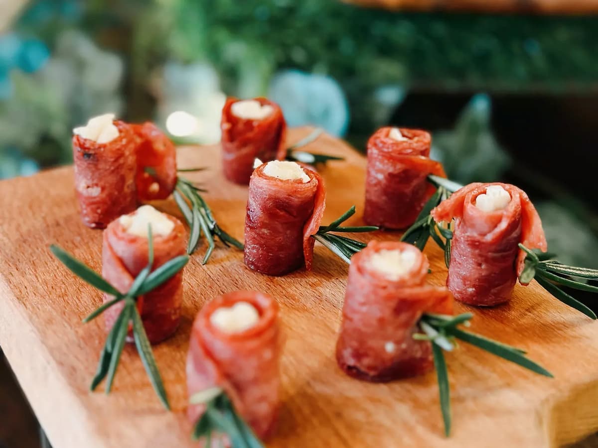 Bite-sized prosciutto-wrapped appetizers with cheese filling and rosemary garnish on a wooden board.
