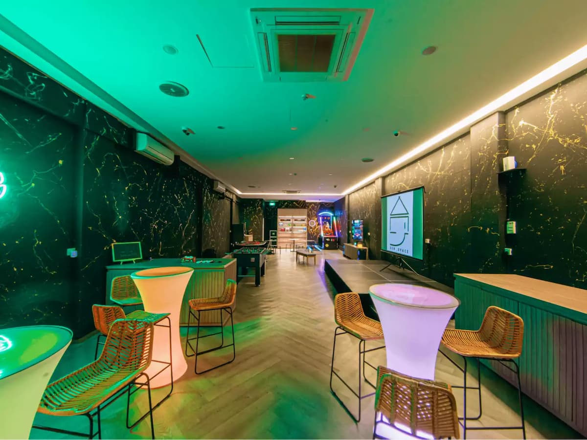 Modern event lounge with cocktail tables, gaming area, and stage setup.