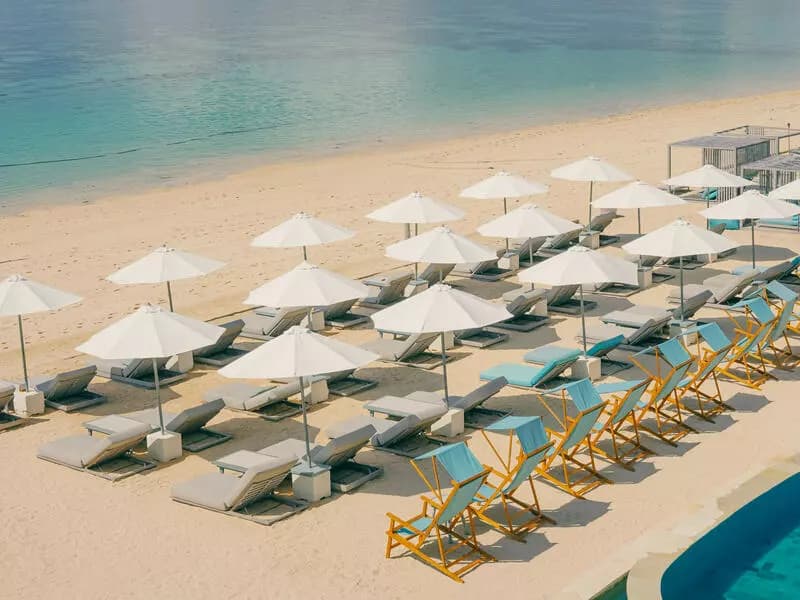 neatly arranged sun loungers, white umbrellas, and vibrant deck chairs at the seaside