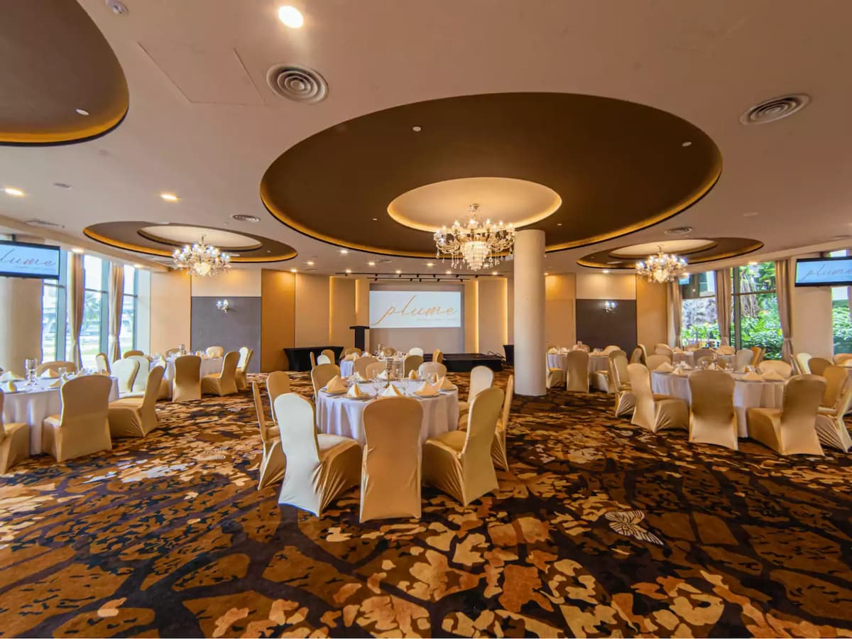 banquet hall with round tables draped in white tablecloths, gold-upholstered chairs, luxurious chandeliers, and a stylish patterned carpet