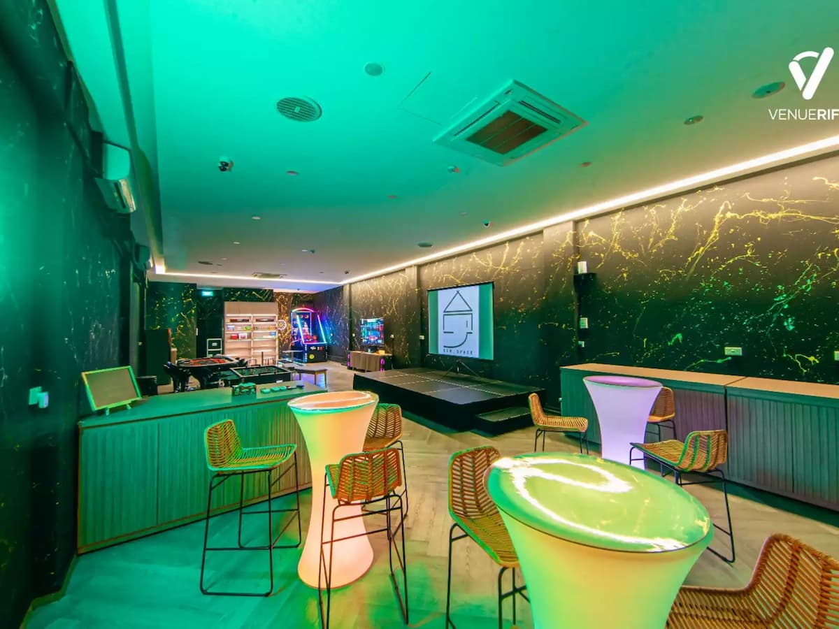 Modern entertainment lounge with cocktail tables, gaming area, and presentation stage.