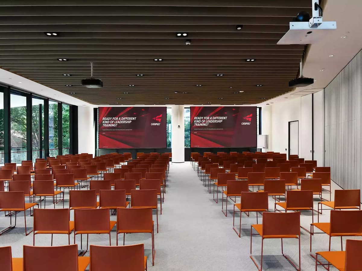 Auditorium setup with theatre-style seating, projection screens, and presentation stage.