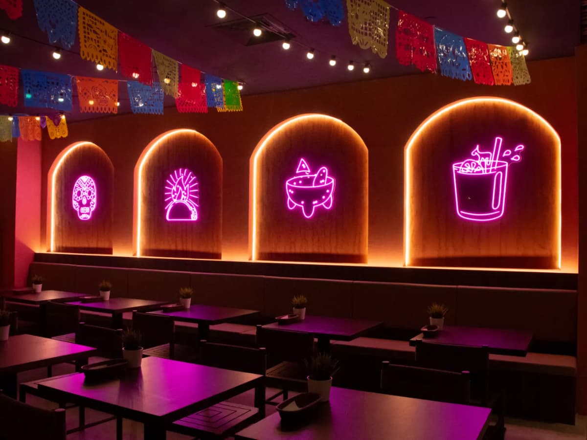 A cozy dining space with glowing neon icons, festive papel picado, and warm ambient lighting