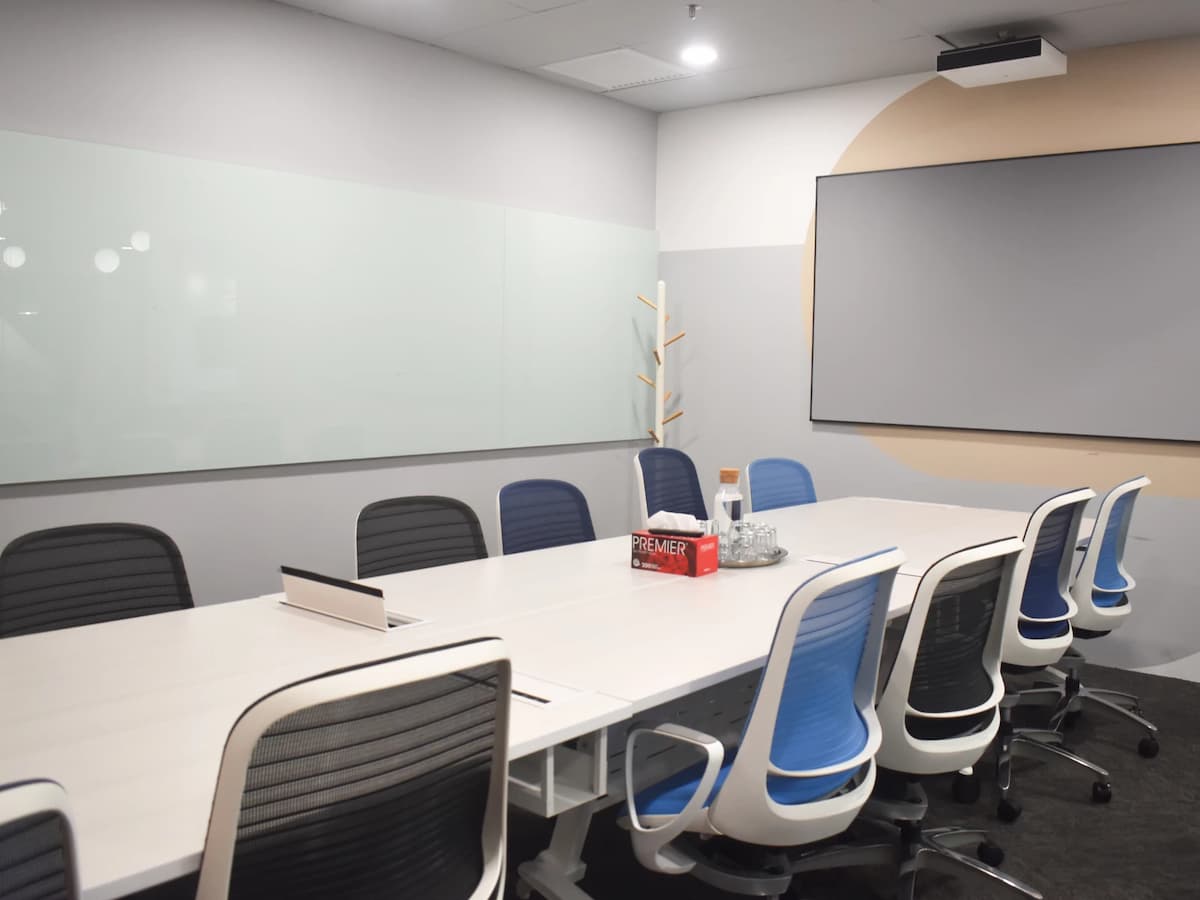 A sleek meeting room with a long white conference table, blue ergonomic chairs, a large wall-mounted screen