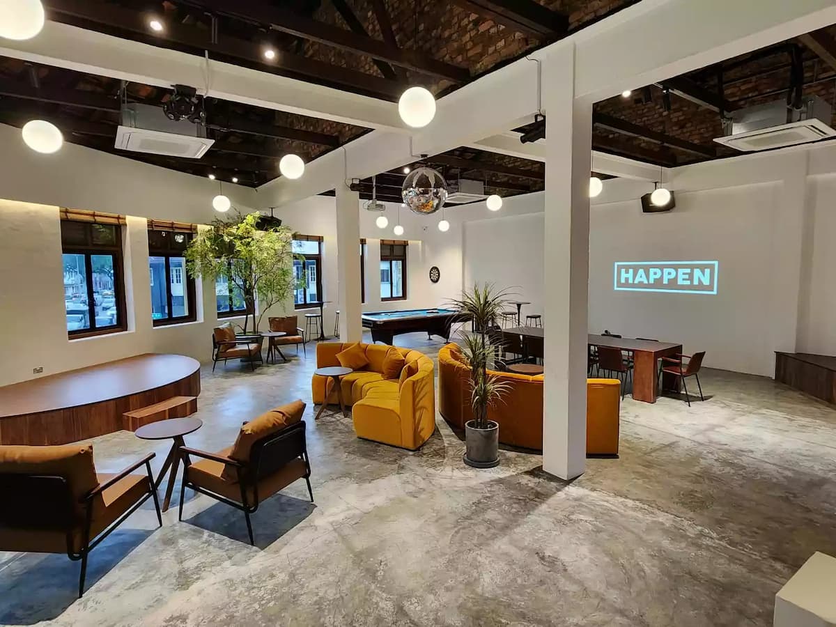 ide-angle view with mustard lounge seating, pool table, indoor plants, globe pendant lights, and a projected brand logo — suitable for private parties or corporate events