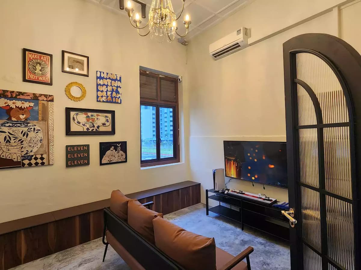 Cosy lounge room with eclectic art gallery wall, leather sofa, flat-screen TV, chandelier, and an arched glass door