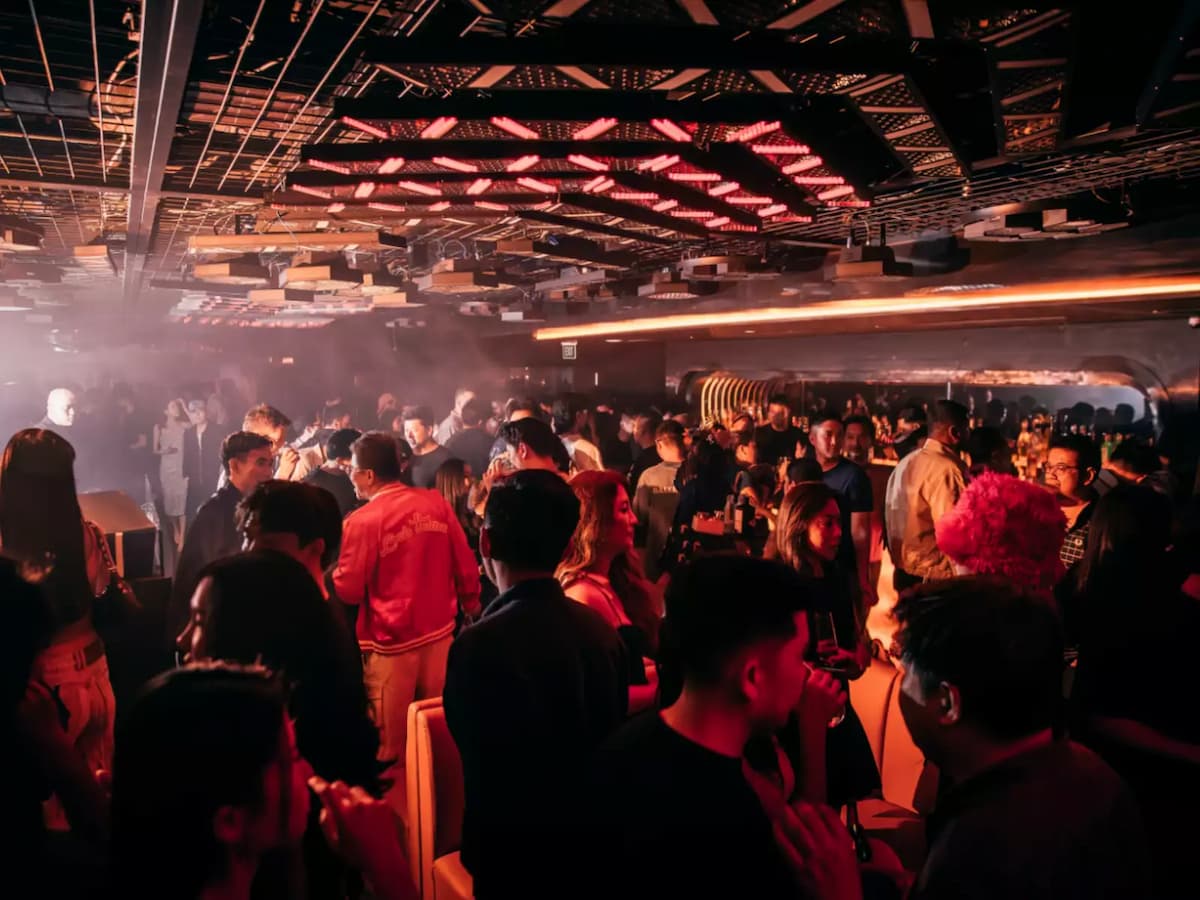 Crowded nightclub with guests socializing under red neon ceiling lights and a vibrant party atmosphere.