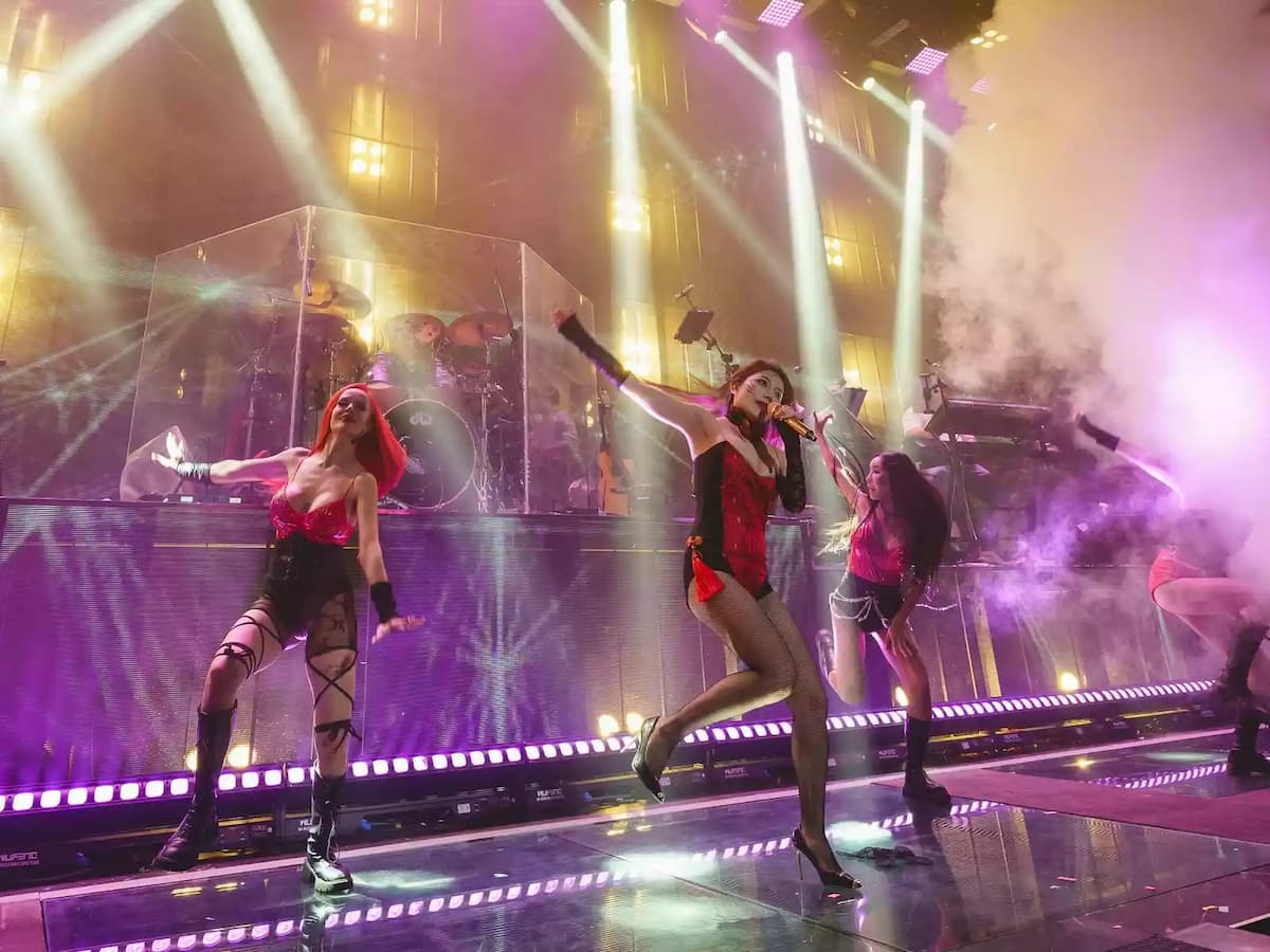 Live stage performance featuring singers, dancers, and a live band under dramatic lighting and stage effects