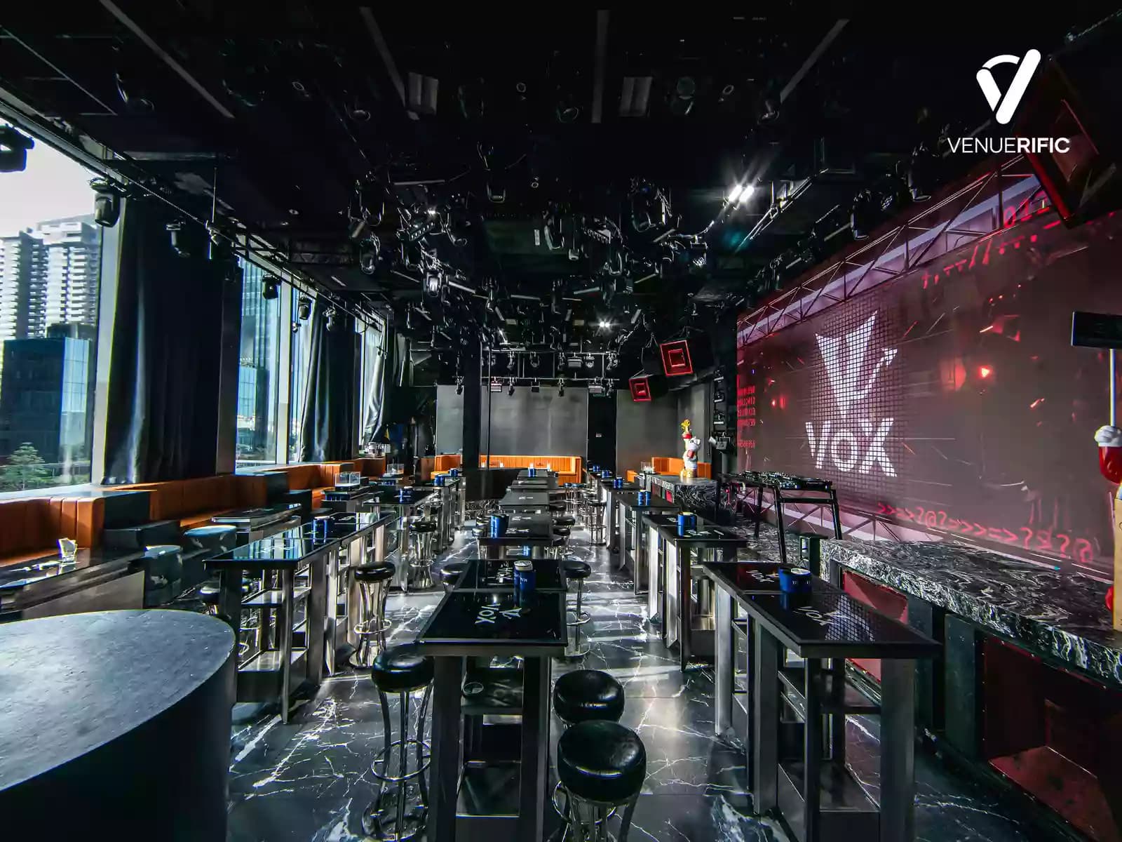 Modern club area with high tables, stage, LED screen display, and floor-to-ceiling windows overlooking the city.