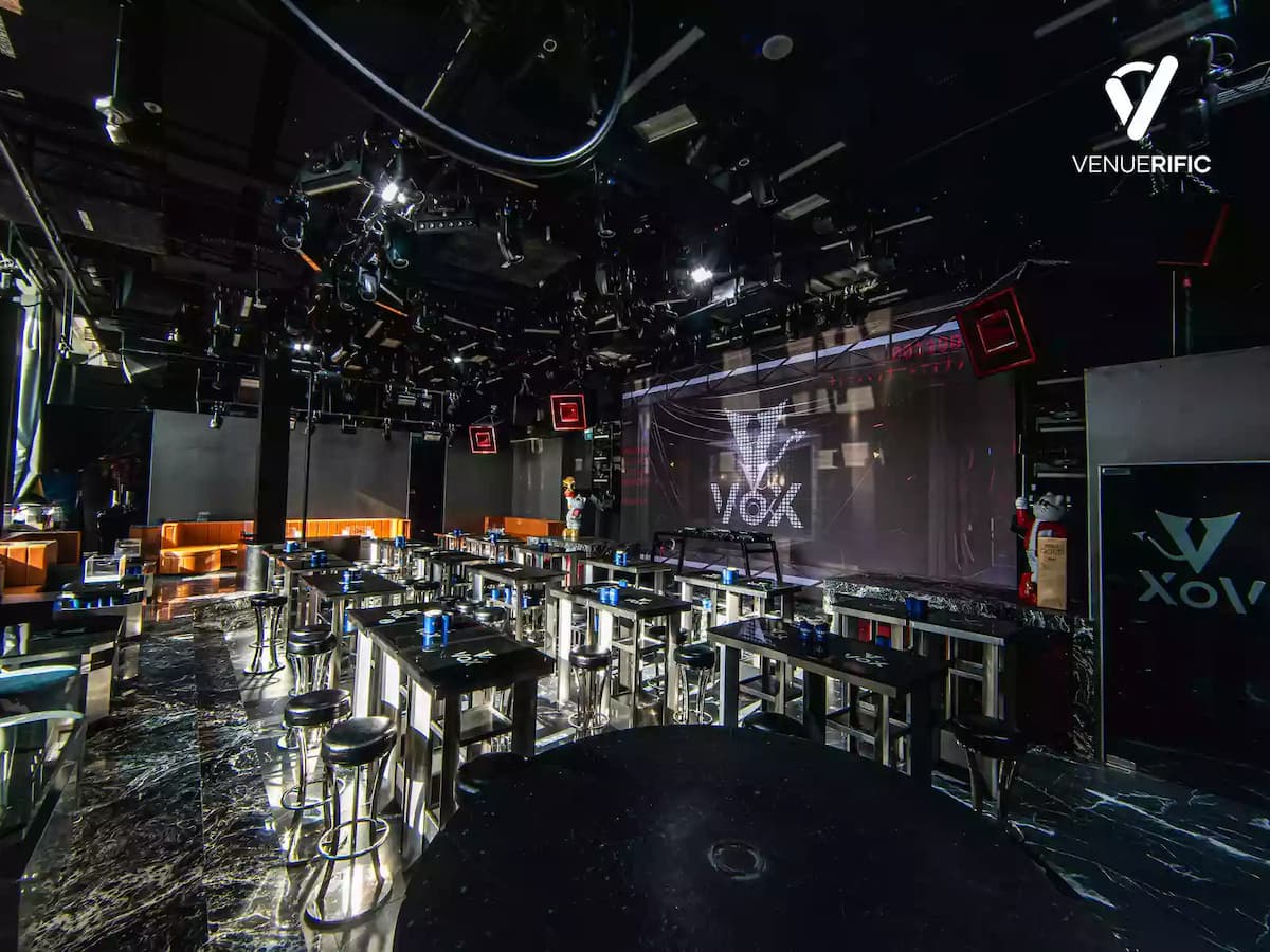 Spacious nightclub venue with high tables, stage, large LED screen, and professional lighting rig.