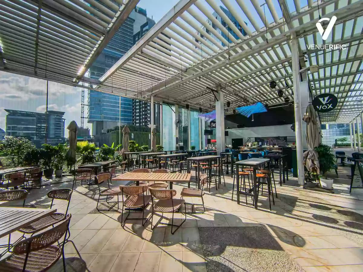 Rooftop venue with wooden deck flooring, bar counter, lounge seating, and a covered pergola overlooking the city skyline.