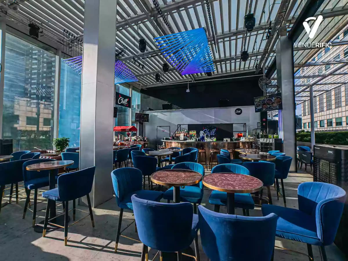 Modern rooftop bar with blue velvet chairs, round marble tables, LED ceiling lights, and a sleek bar counter.