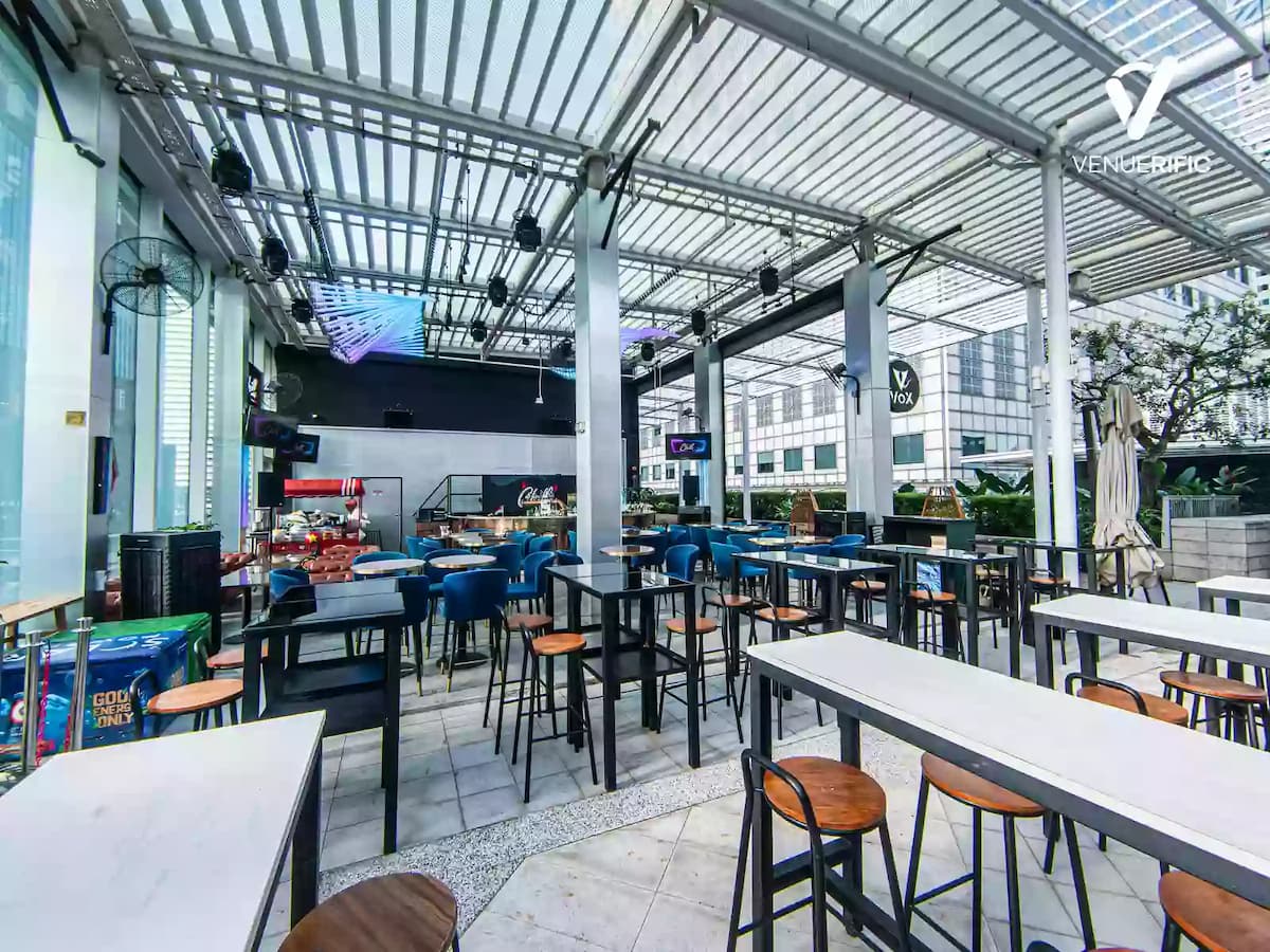Spacious rooftop event space with high tables, blue chairs, bar area, and covered pergola with city views.