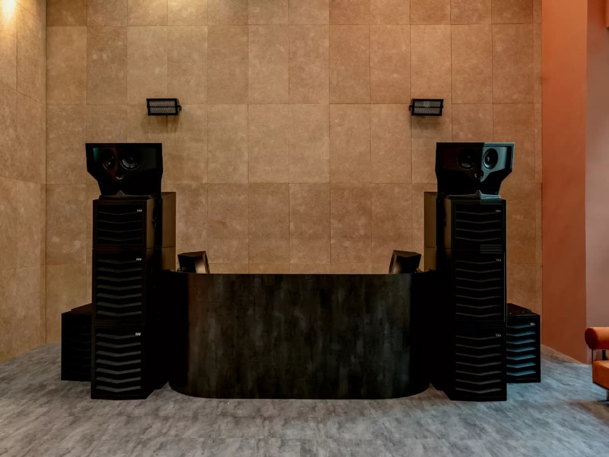 DJ booth setup with large speakers against a tiled wall backdrop.