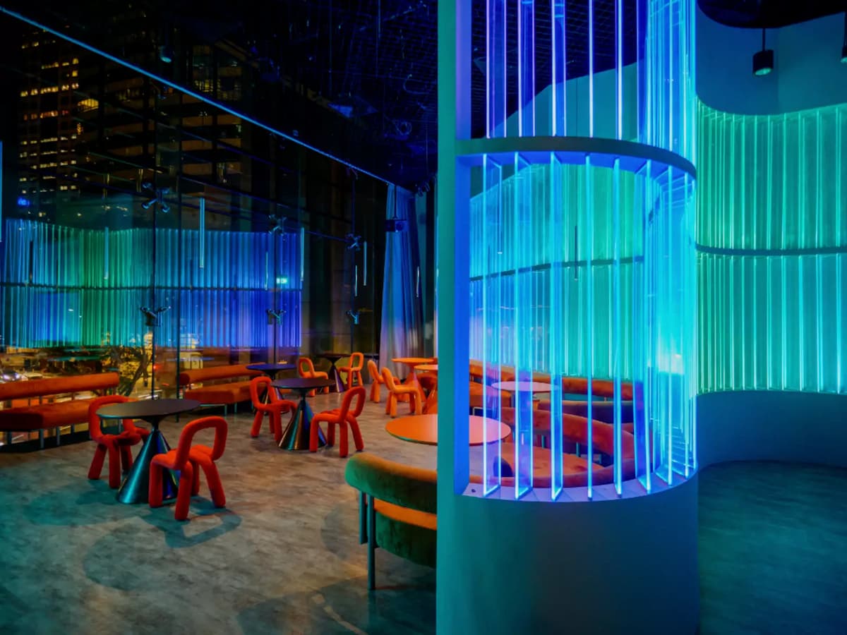 Modern lounge with neon-lit cylindrical feature, red chairs, and city skyline views through glass walls.