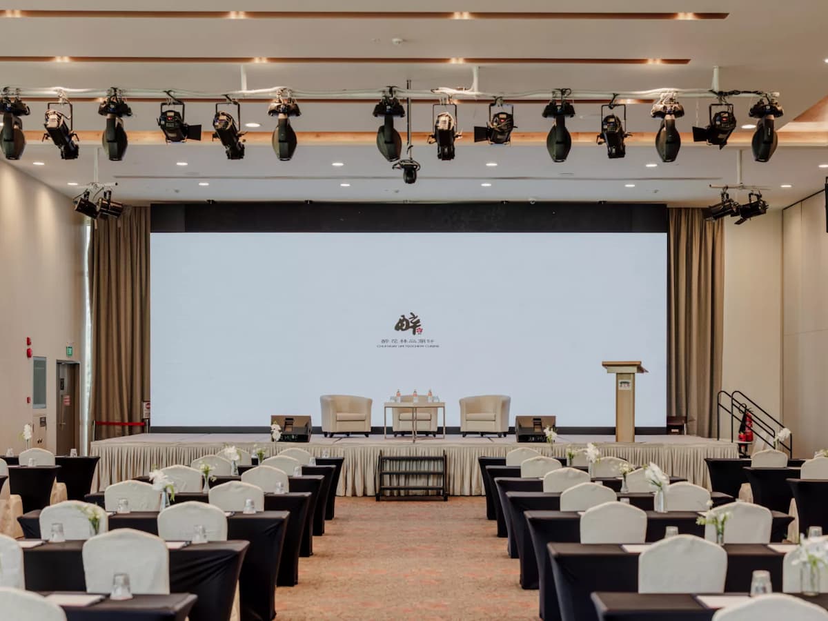 Conference room with rows of tables and white chairs facing a stage.