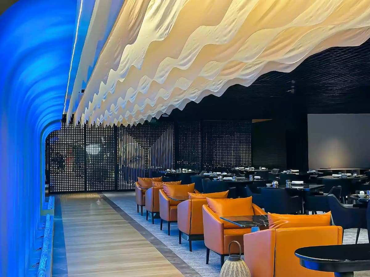 Contemporary dining venue with wave ceiling, lounge seating, and modern lighting.