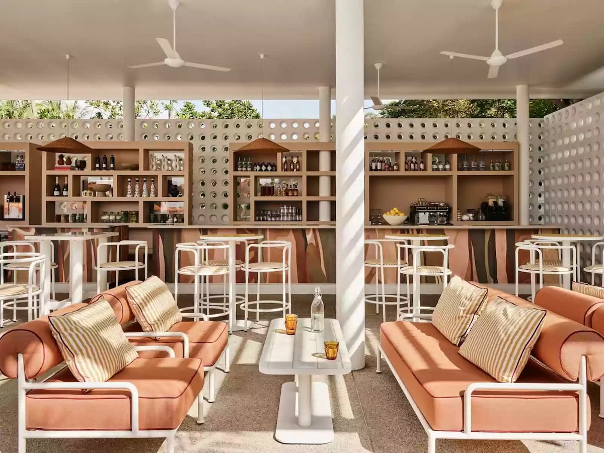 Open-air area with cushioned seating, white bar stools, and wooden shelves stocked with drinks behind the counter.