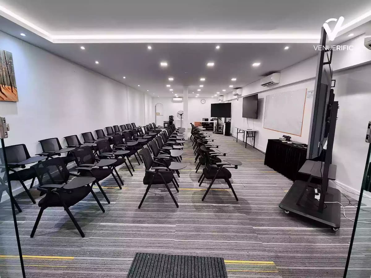 Modern training room with rows of black chairs facing a whiteboard and two large flat-screen monitors.